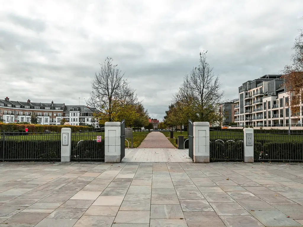 The entrance to Imperial park, with a straight path through it lined with small trees. There are apartments on the right side of the park and on the other side to the left. 