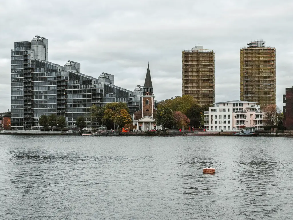 Looking across the water of the River Thames to St Mary's Church on the other side. The church is surrounded by multiple apartment buildings. 