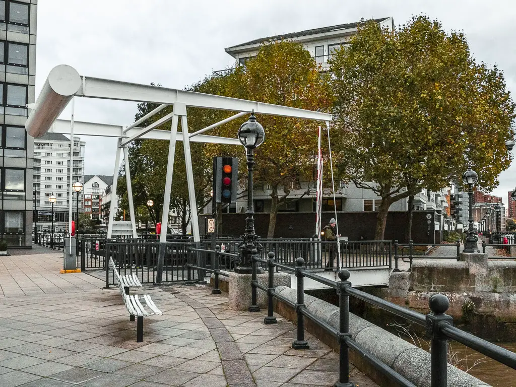 Traffic lights over a small bridge which leads to Chelsea Harbour. A man is walking over the bridge. 