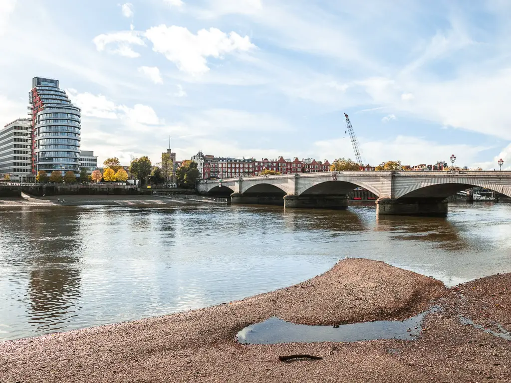 Looking across the bank of the river at low tide, with Putney Bridge crossing the river on the Thames Path walk towards Battersea. 