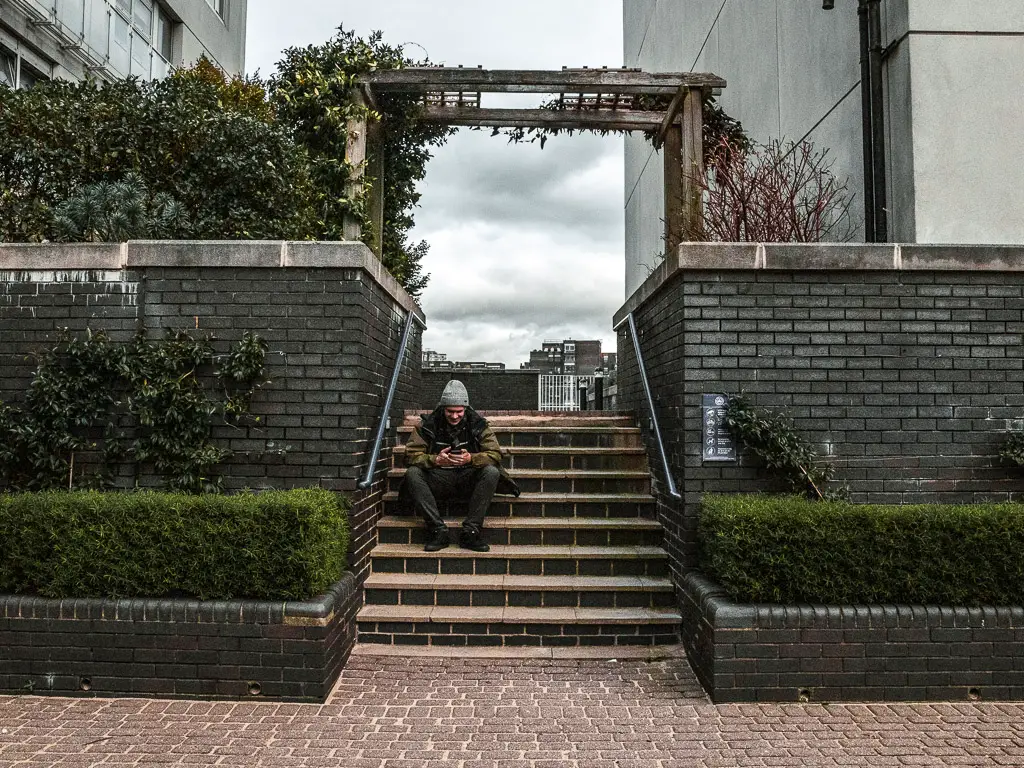 A man sitting on some steps which lead up and through a gap in the apartment buildings. 