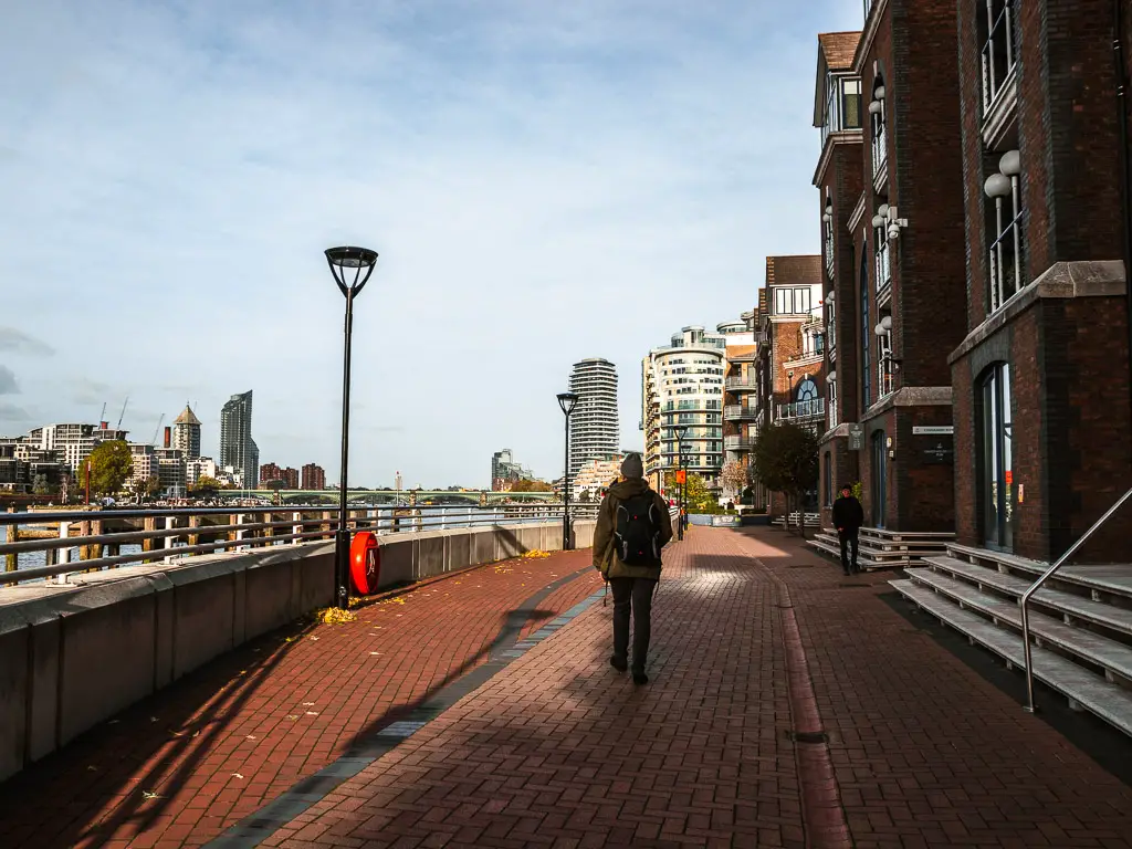 A man on a walk along the wide Thames Path in Battersea halfway in the walk from Putney.