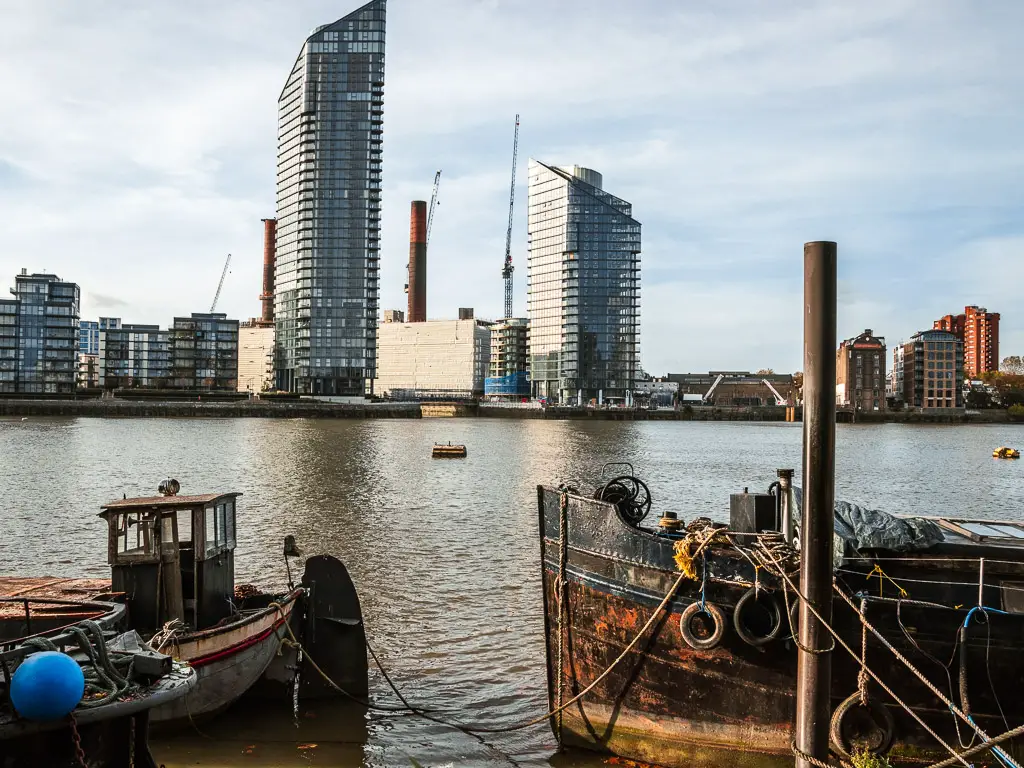 The old boats on the River Thames, and tall apartment buildings on the other side. 