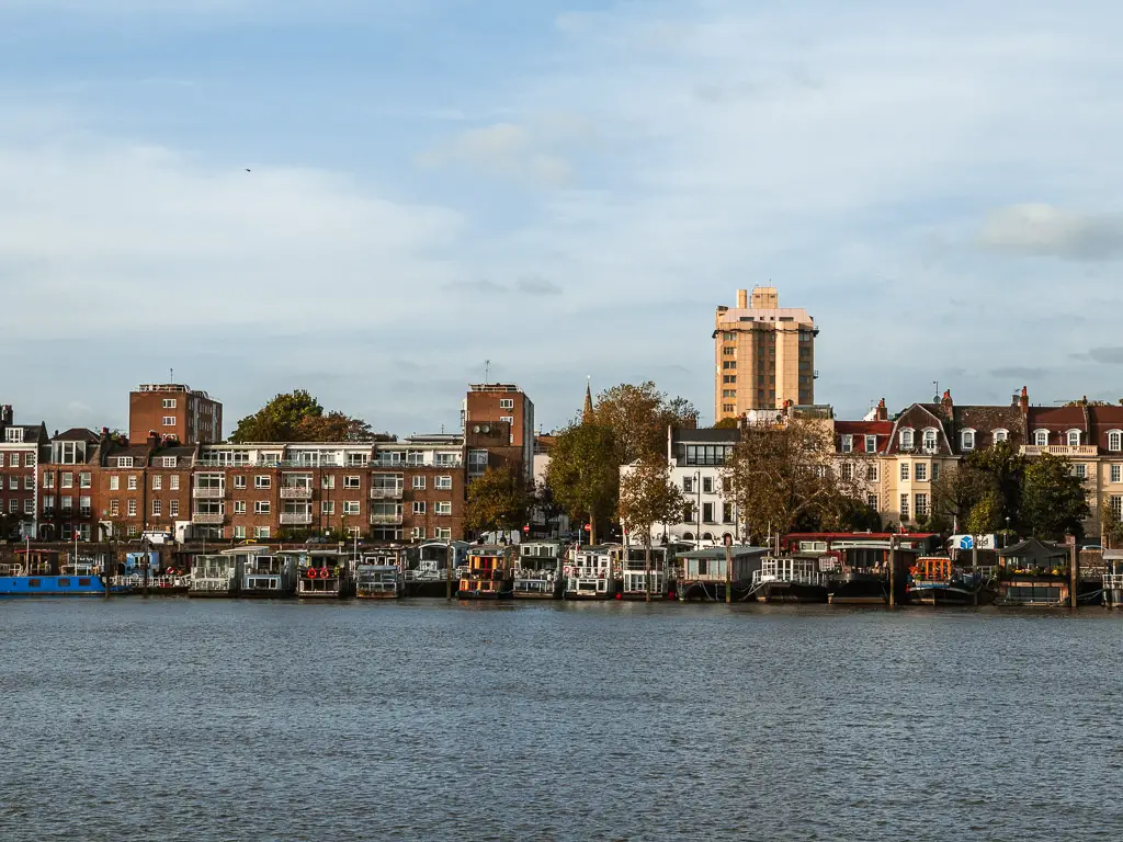 Looking across the river to the house boats and buildings on the other side, on the Thames Path walk from Putney to Battersea. 