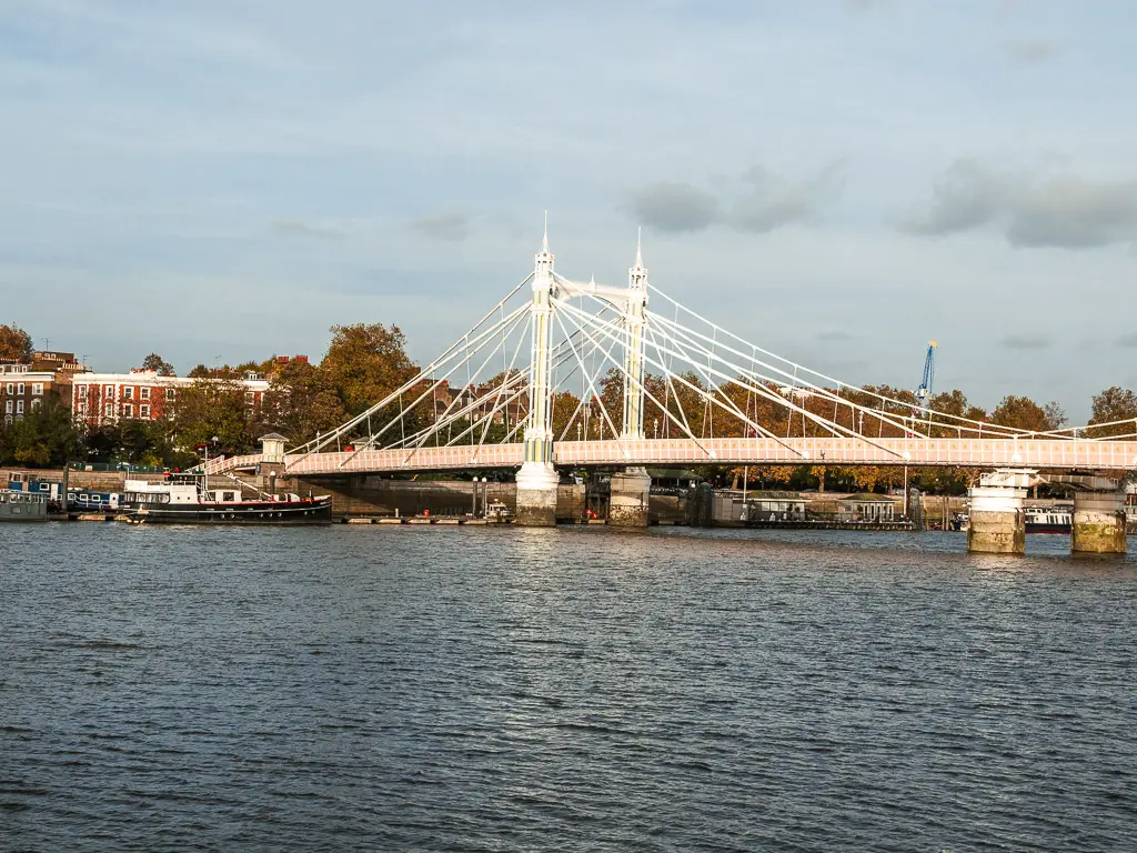 Looking across the River Thames towards the white and pink coloured Albert Bridge at the end of the walk from Putney to Battersea along the Thames Path.