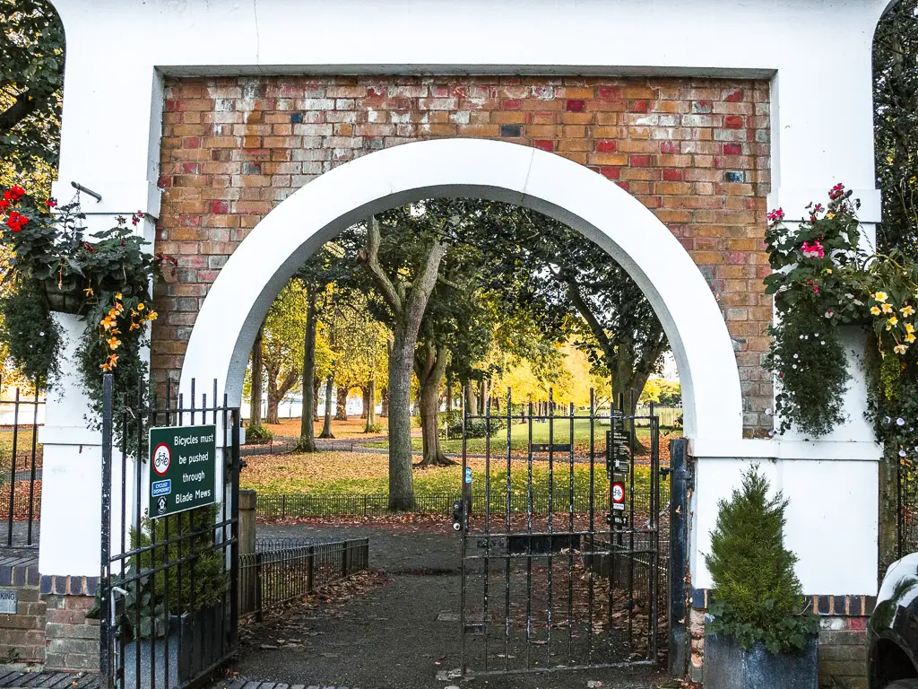 Looking through the brick archway and black iron gate to the green of Wandsworth park.