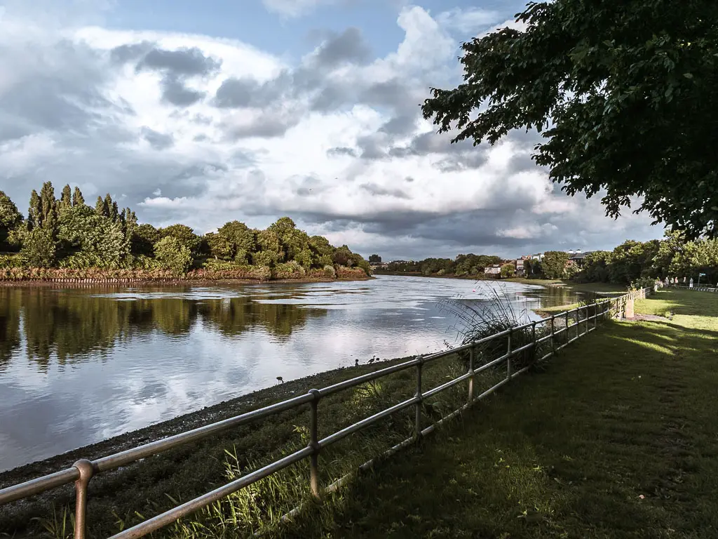 Looking down the river, with a green to the right and lots of trees on the left on the other side of the river. 