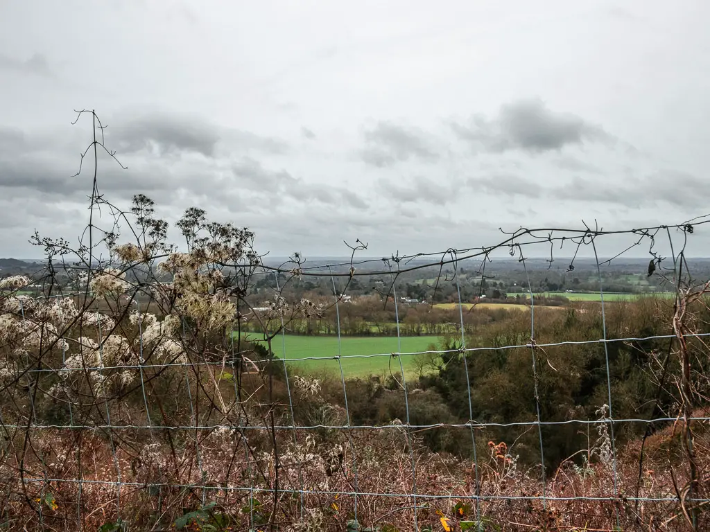 looking through the wire fence to the green fields in the distance on the walk from Westhumble to Merstham.