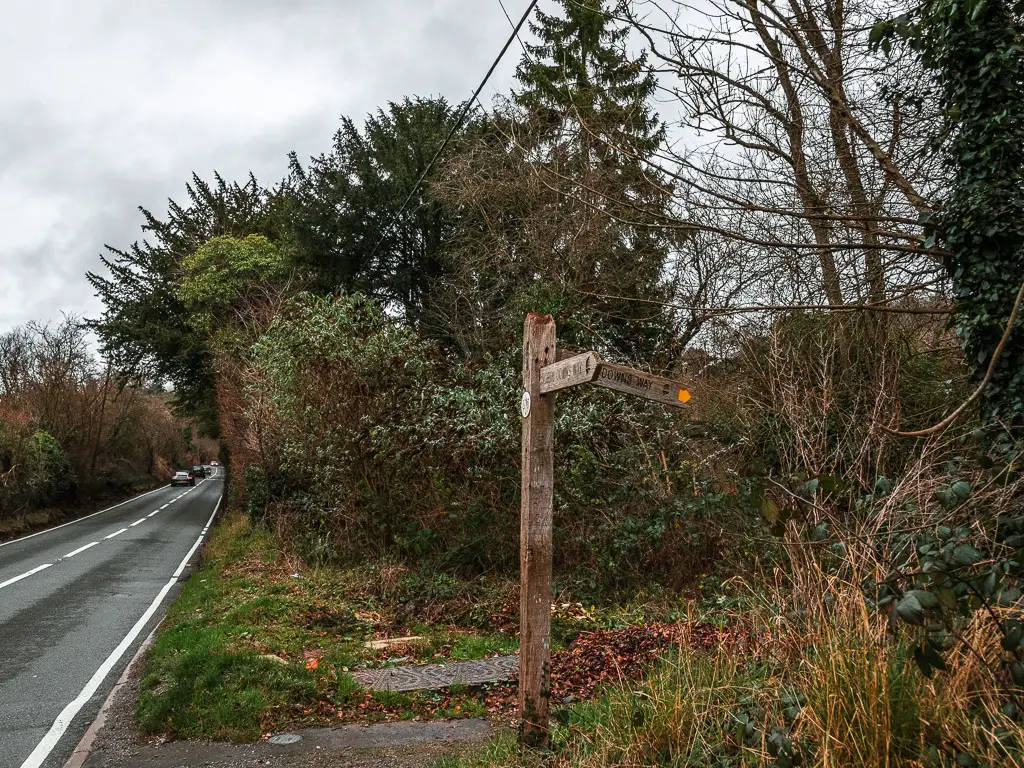 A wooden signpost on the side of the road, pointing to the right into the woodland.