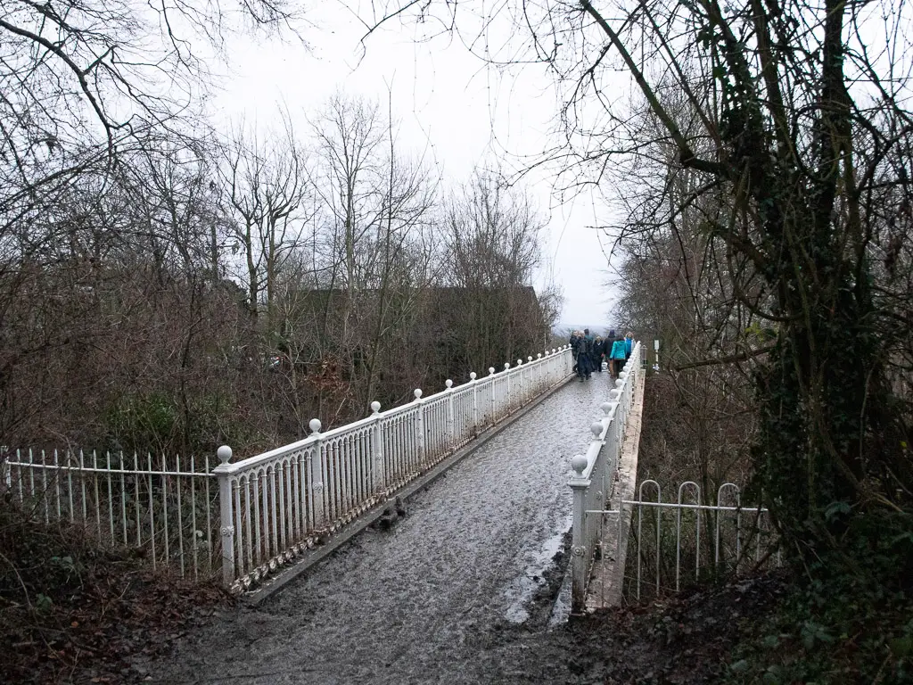 A white metal bridge with a few people walking across it on the walk from Westhumble to Merstham, along stage 3 of the North Downs Way.