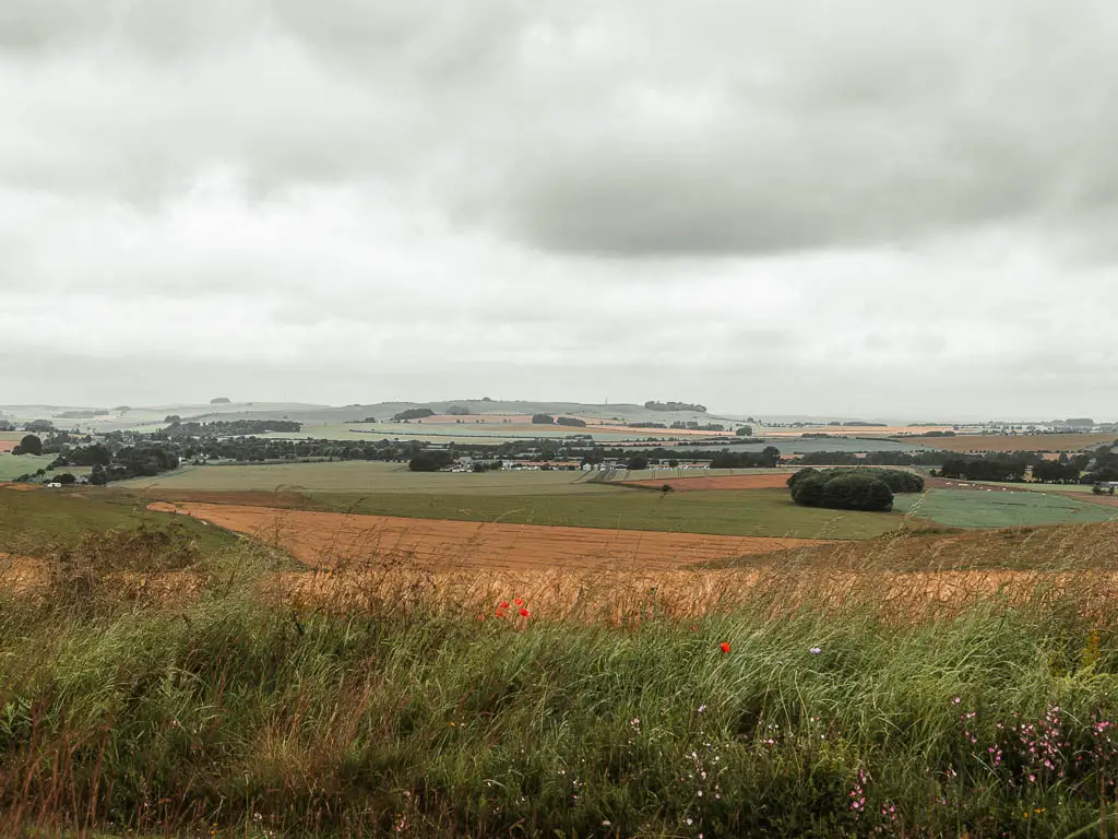 A distant view across the orange and green patchwork fields in North Wessex on the walk towards Avebury from Hackpen Hill.