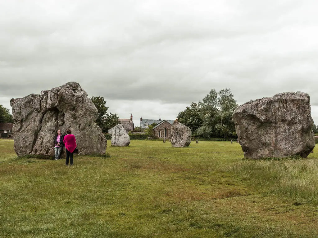 Large stones in a field in Avebury on the hallway point on the walk from Hackpen Hill along the Ridgeway. There are a couple of people standing in front of one of the stones.