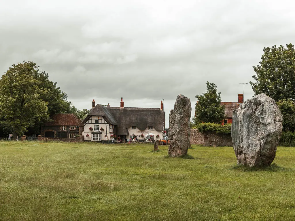 Two large stones in a field in front of a thatched roofed cottage in Avebury on the walk from Hackpen Hill.