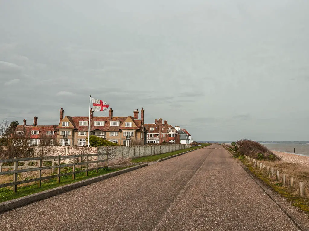 A road with some buildings and the St George's flag on the left, and the shingle beach and English Channel on the right.