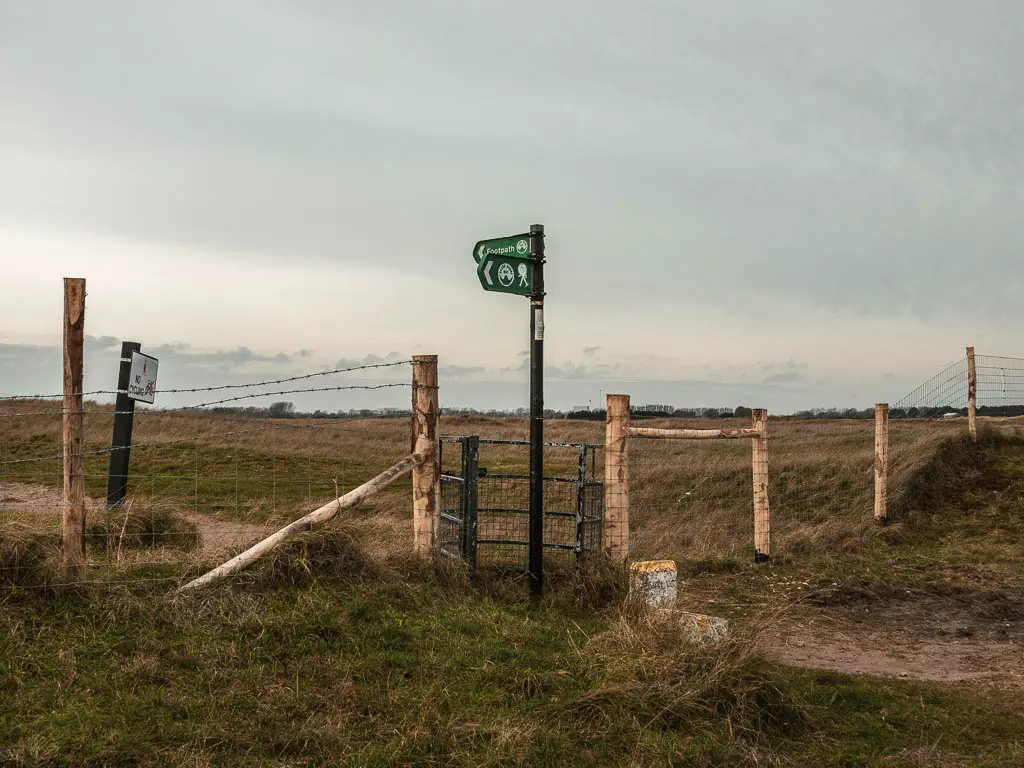 A green signpost next to a barbed wire fence in front of the golf course. 