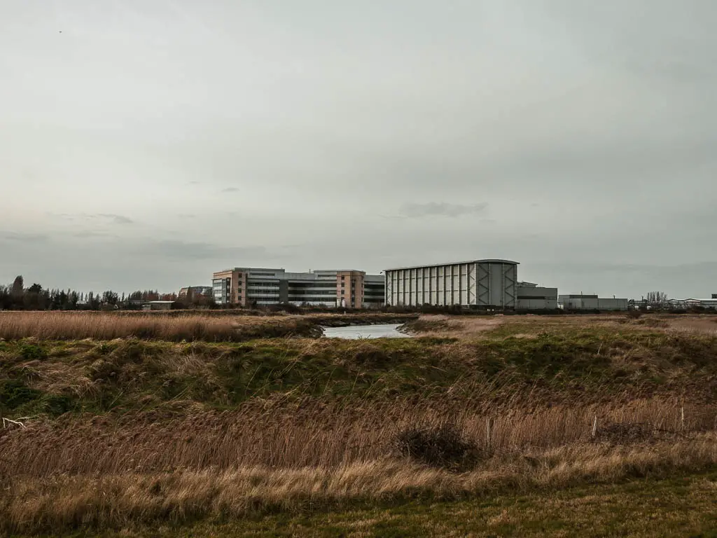 looking across the hay and green towards some industrial buildings. The River Stour is just visible. 