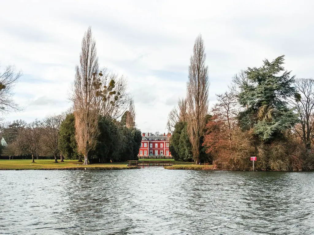 A red mansion visible through the trees on the other side of the River Thames on the walk from Henley to Marlow.