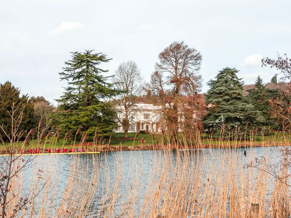 The River Thames with a green on the other side with large trees and a big white manor house behind them.