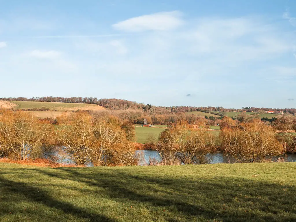 Looking down the grass hill towards the River Thames and green fields and hills on the other side on the walk from Henley to Marlow. 