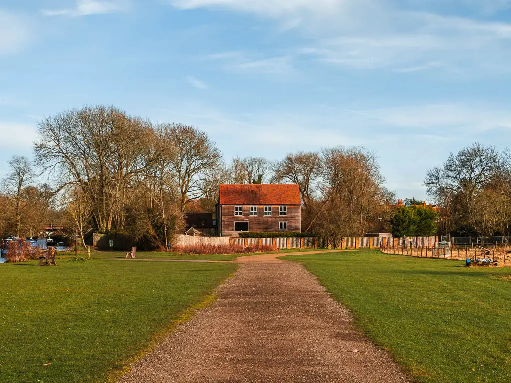 A wide path leading towards a wooden budding with a red roof on the walk from Henley on Thames to Marlow. 