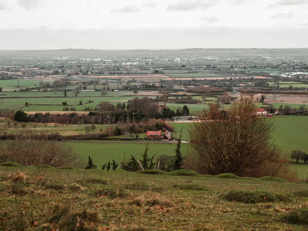 A view down to green fields as far as the eye can see on the walk from Wendover to Coombe Hill and Beacon Hill. There is a lonely red roofed house on the flat at the bottom of the hill.