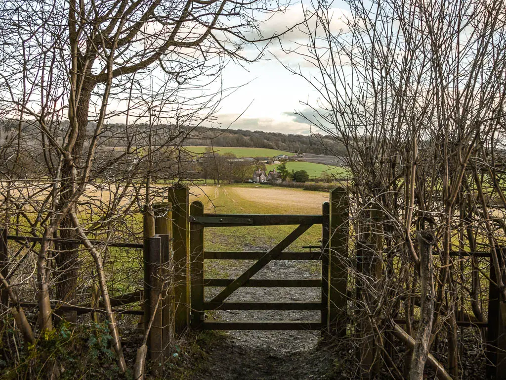 A wooden gate leading to a large green field, with hills in the distance. 