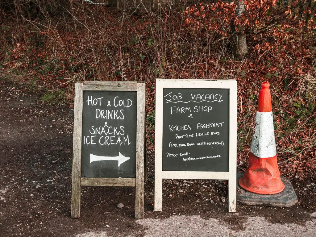 Two chalk boards next to a red traffic cone. The chalk board writing points to a farm shop with snacks, drinks and ice cream. 