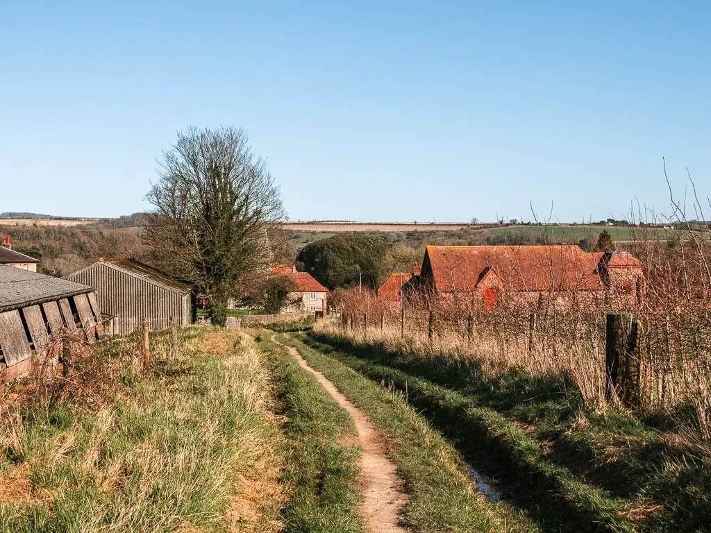 A narrow trail leading downhill with brick and flint houses ahead on the walk from Amberley to Arundel.