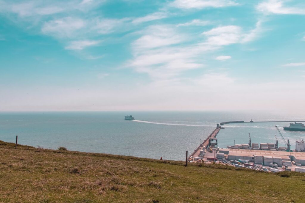 Looking out to the English Channel beyond the green grass field. There is a a ferry in the distance heading towards France.