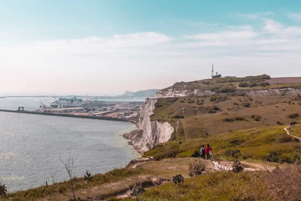 Looking across the undulating grass clifftop on the white Dover Cliffs, on one of the coastal walks near London. There are a couple of people walking along the trail on the clifftop.