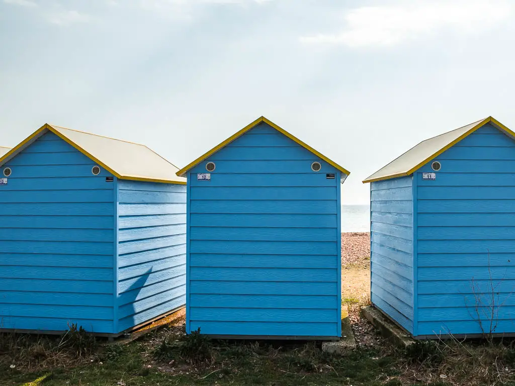 Three blue beach huts with yellow roofs on the walk to Worthing from Littlehampton. 