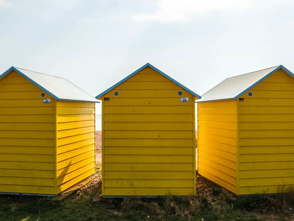 Three yellow beach huts on the coast oath walk to Littlehampton to Worthing. 