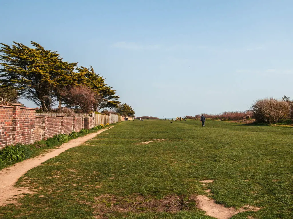 A large green with a brick wall to the left. there is one person walking on the green. 