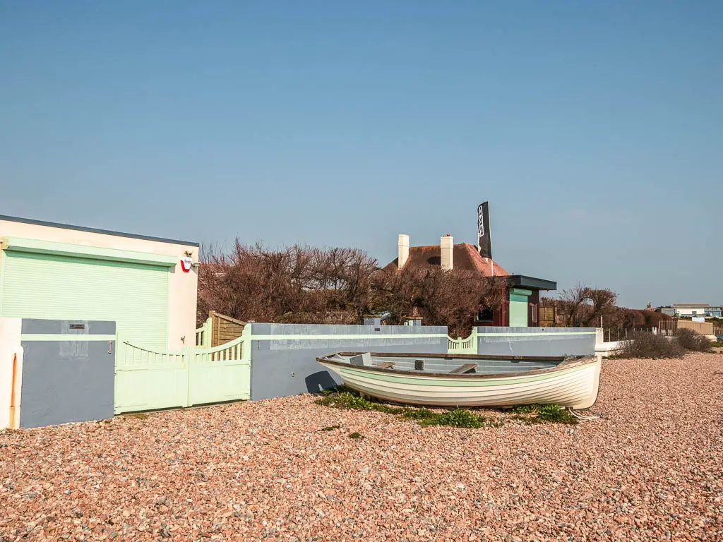 A white and pastel coloured row boat on the shingle on the coastal walk from Littlehampton to Worthing. 