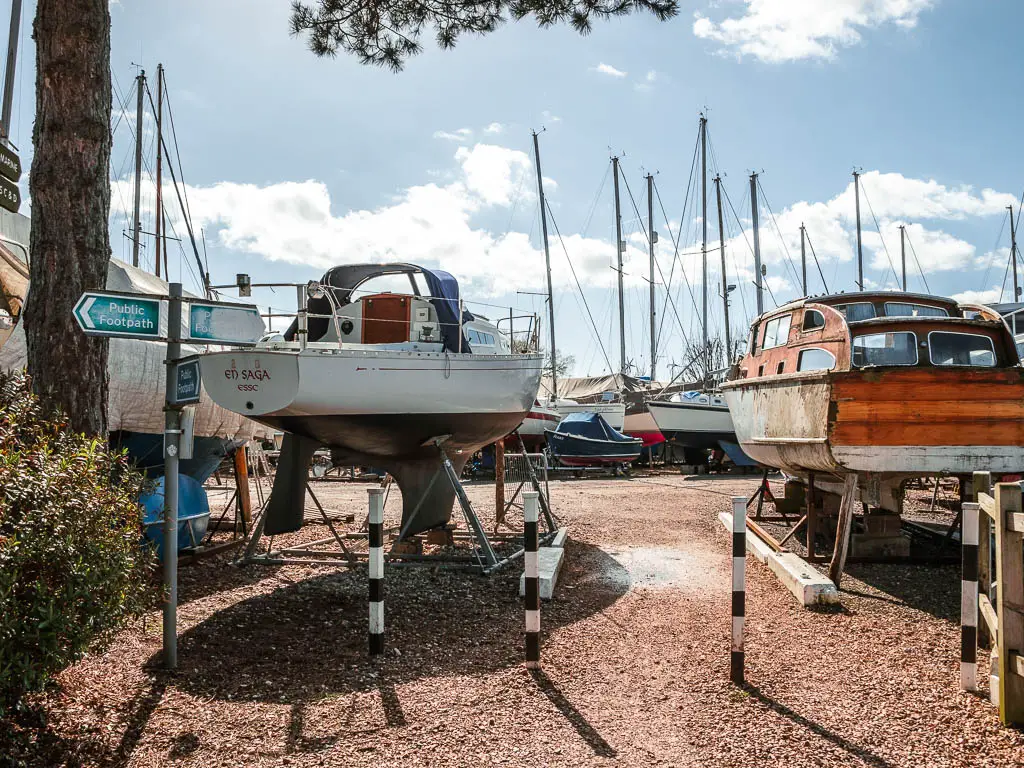 Walking into a boat yard. There is a white boat on the left and a red one on the right.