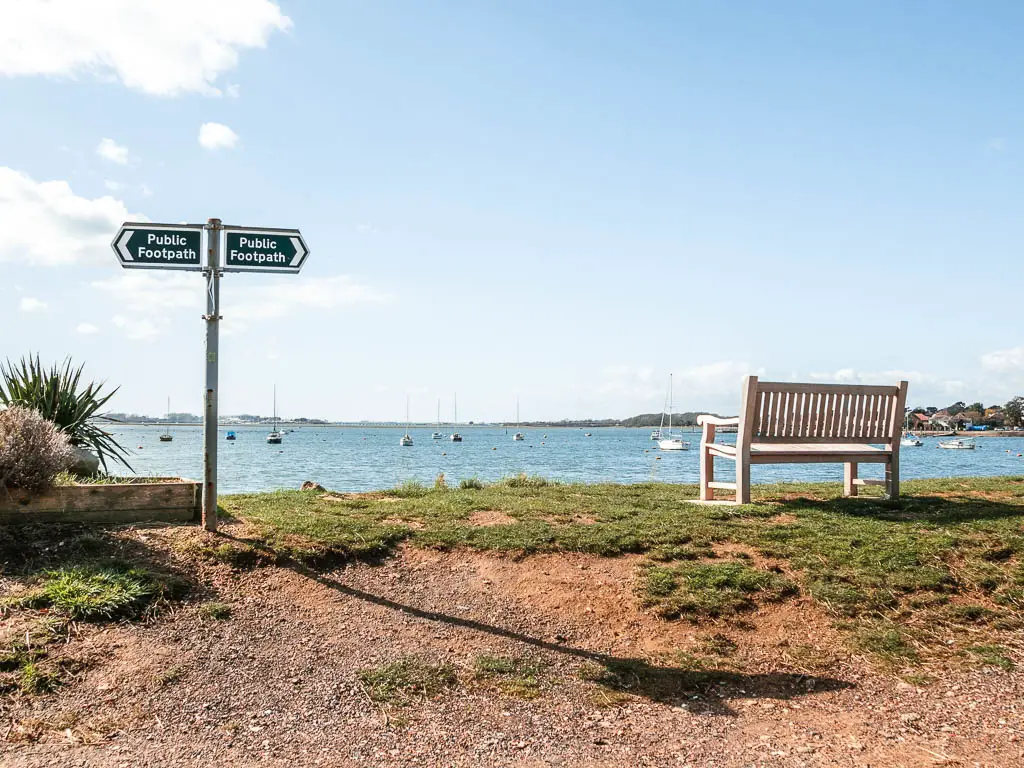 A wooden bench facing the sea and a green 'public footpath' sign on the left. 