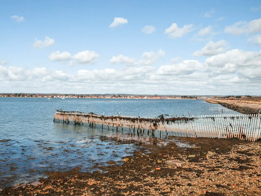 White fencing leading from the land to the blue sea. There is some seaweed on the fence. 