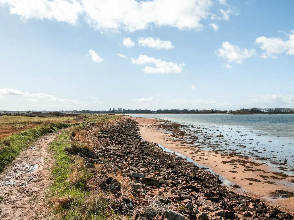 The coast path on the left and rocks and sand on the right leading to the sea on the walk around Thorney Island.