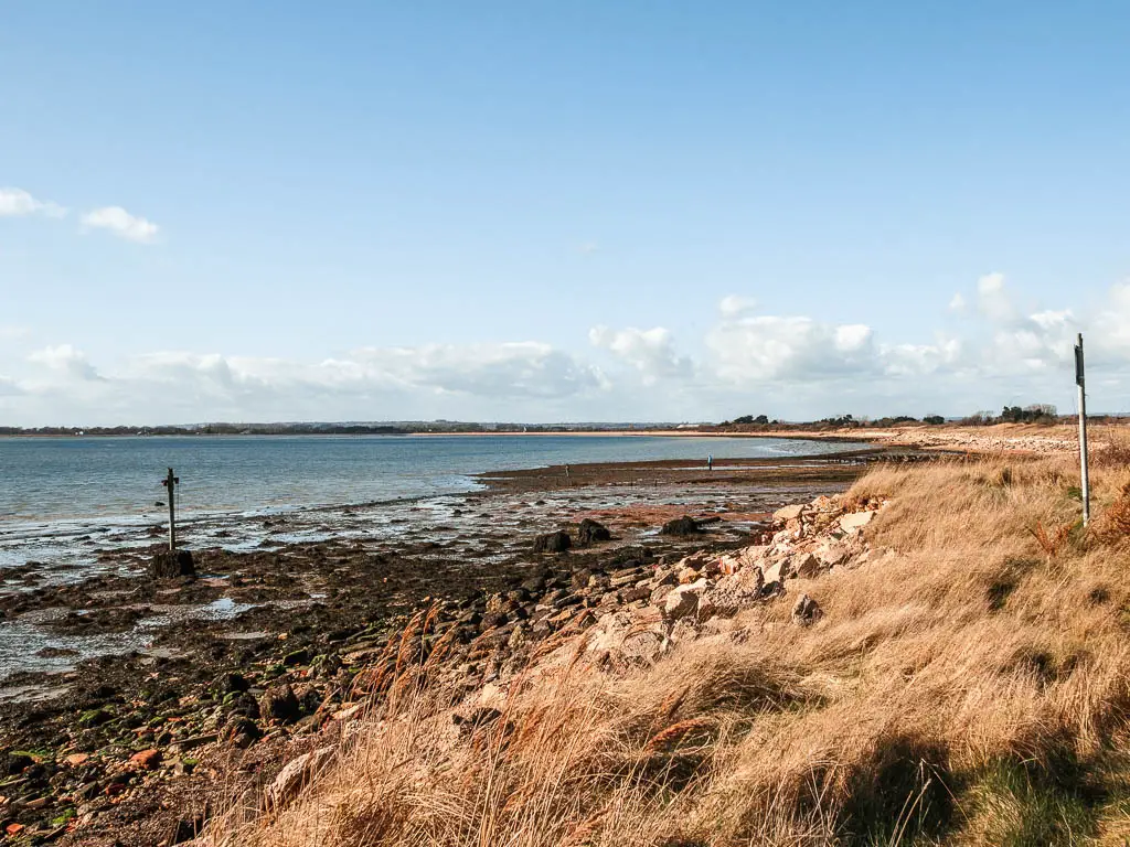 Looking across the long grass and rocks to the sea on the Thorney island walk. 