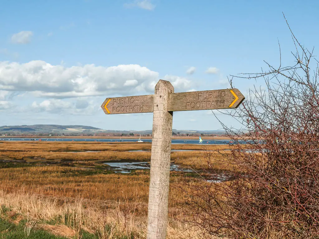 A wooden 'public footpath' signpost infant of the marshland.