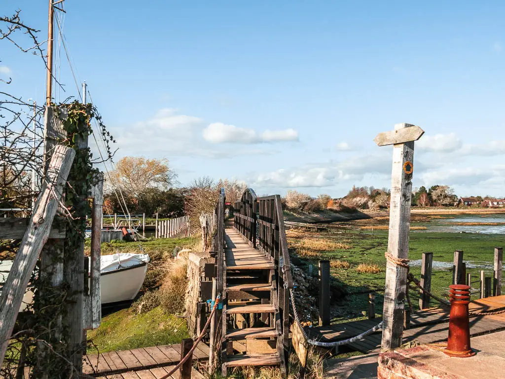 A narrow wooden bridge leading over the sea bed during low tide.