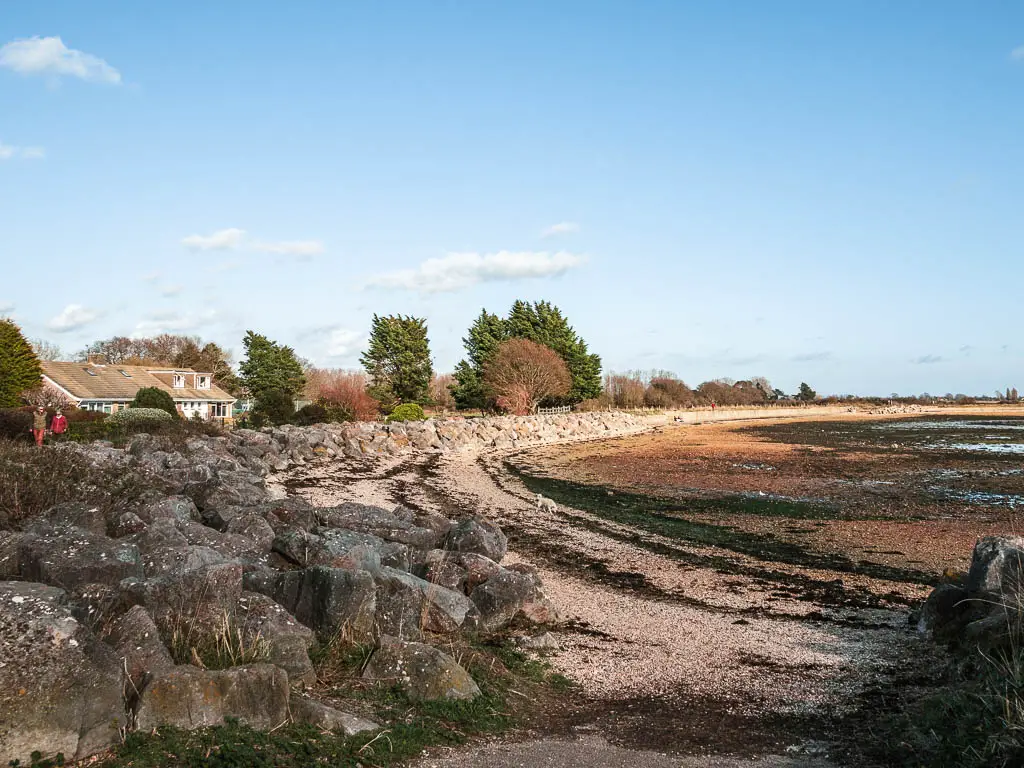 Large rocks curving around the left with the shingle beach in front leading to the sea bed at low tide. 