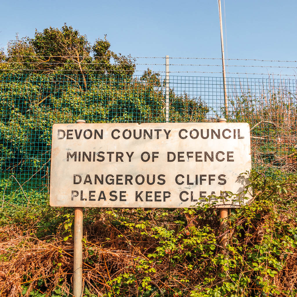 A big rectangle side saying Devon county council, MOD dangerous cliffs, please keep clear.