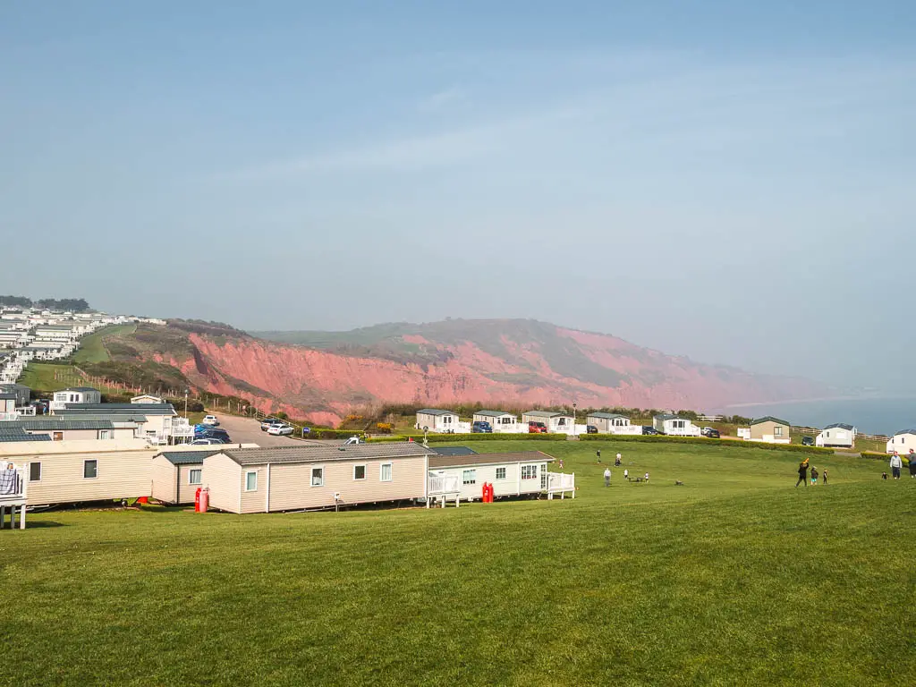 A large area of grass with the holiday park homes and rede cliffs on the other side.