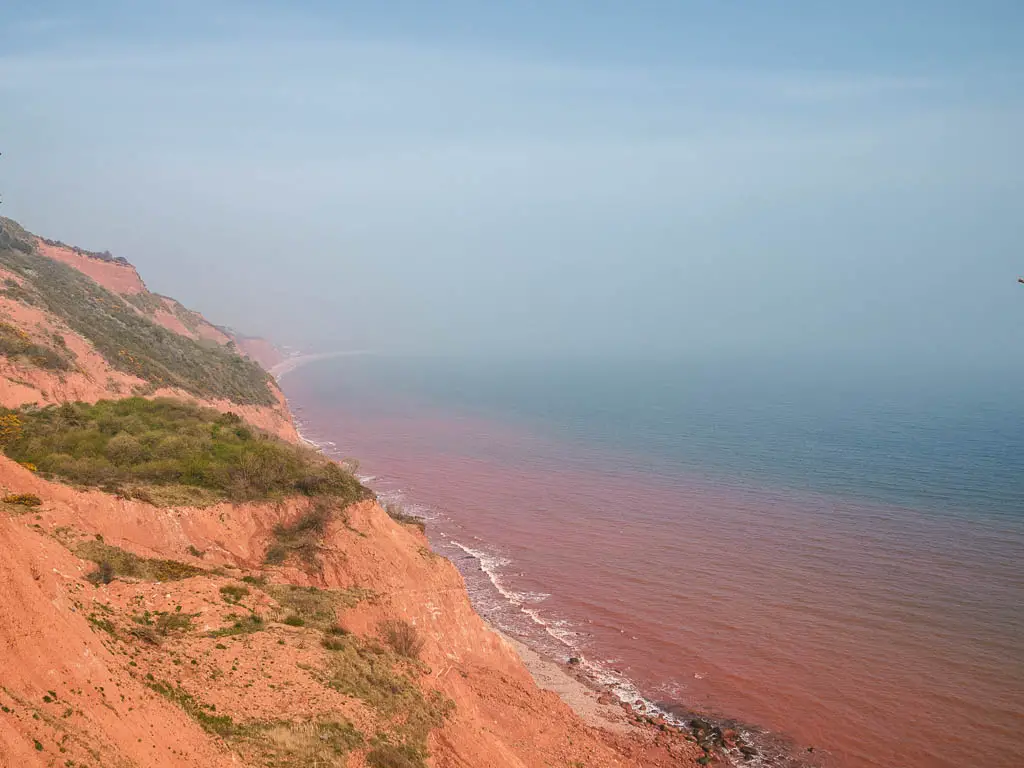 Red cliffs on the left leading down to the red coloured sea on the coastal walk from Exmouth to Budleigh Salterton.