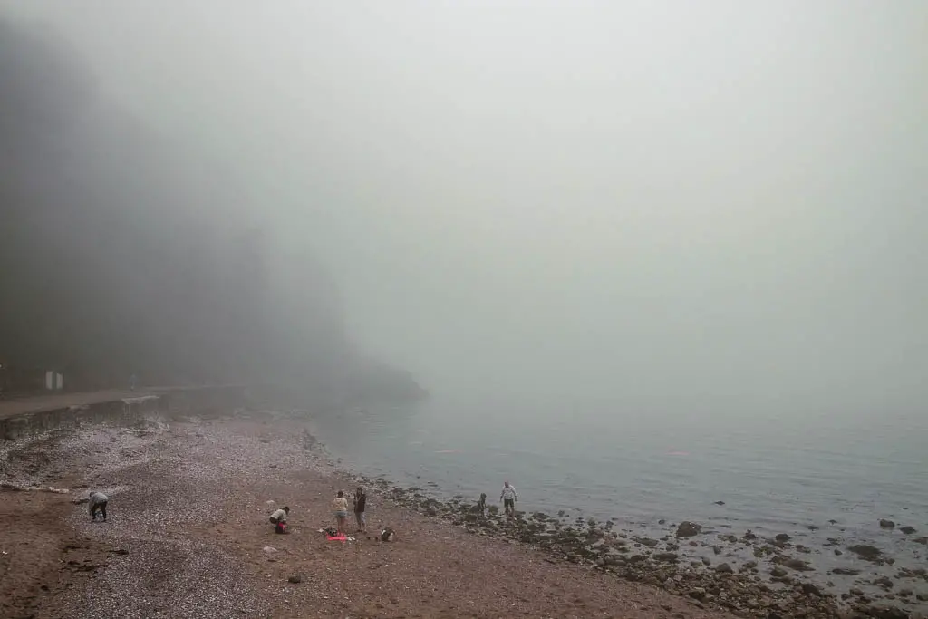 A barely visible beach at Babbacombe, on a very misty foggy day. There are a few people on the beach.