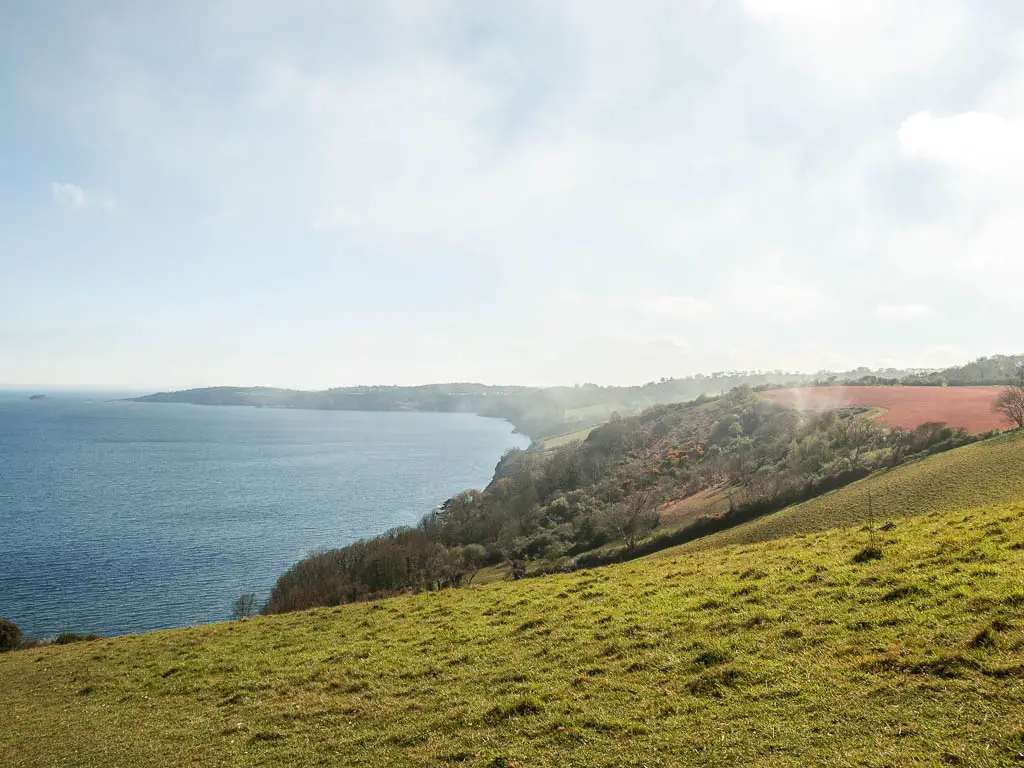 Looking across the grass clifftop to the coastline in the distance, on the Babbacombe to Teignmouth walk. There is mist and fog hanging in the air.