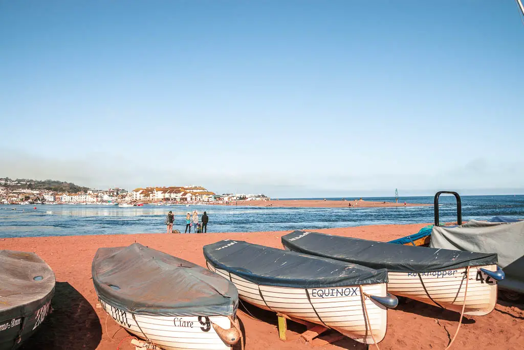 A few row boats lined up on the red sand Shaldon Beach at the end of the walk from Babbacombe.