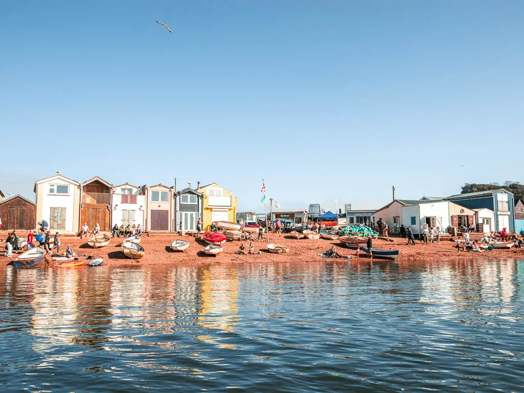 Looking across the water to the beach with a few boats on the sand and some beach huts in Teignmouth.