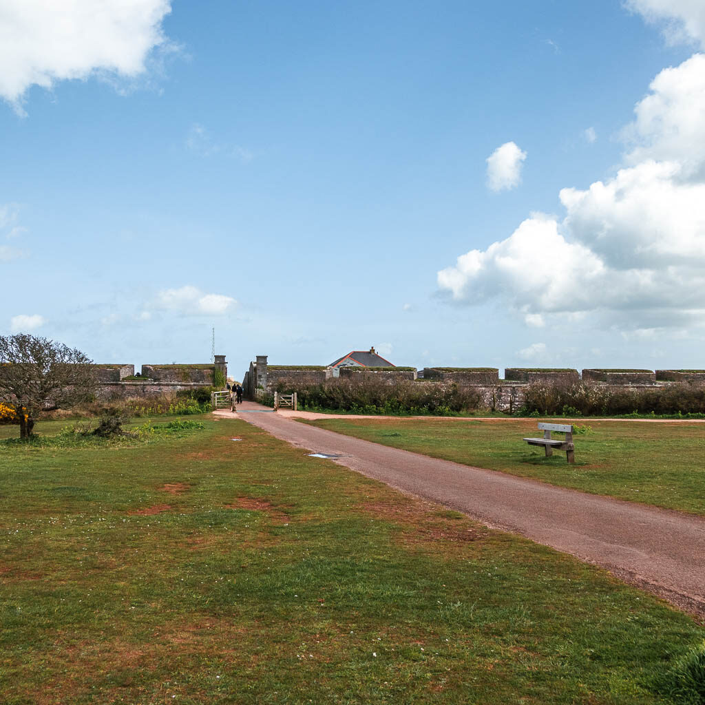 A large green with a path running diagonally though it towards the stone wall.